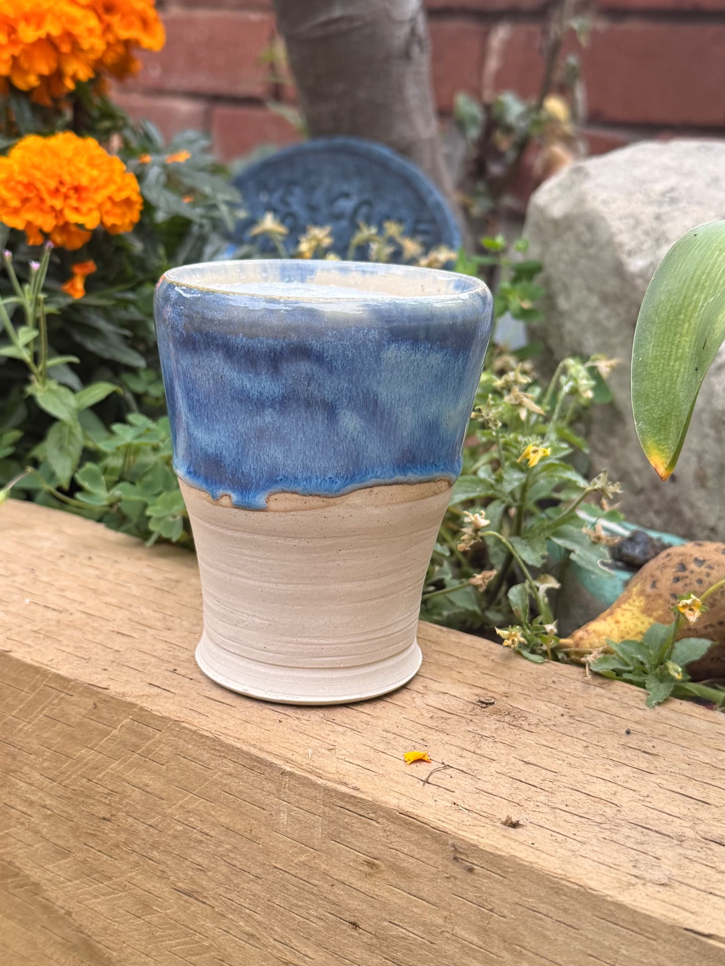 A blue-glazed tumbler on raw clay standing among the marigolds