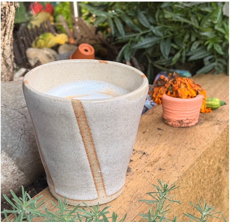 A speckled white tumbler with a raw clay stripe, photographed in the garden